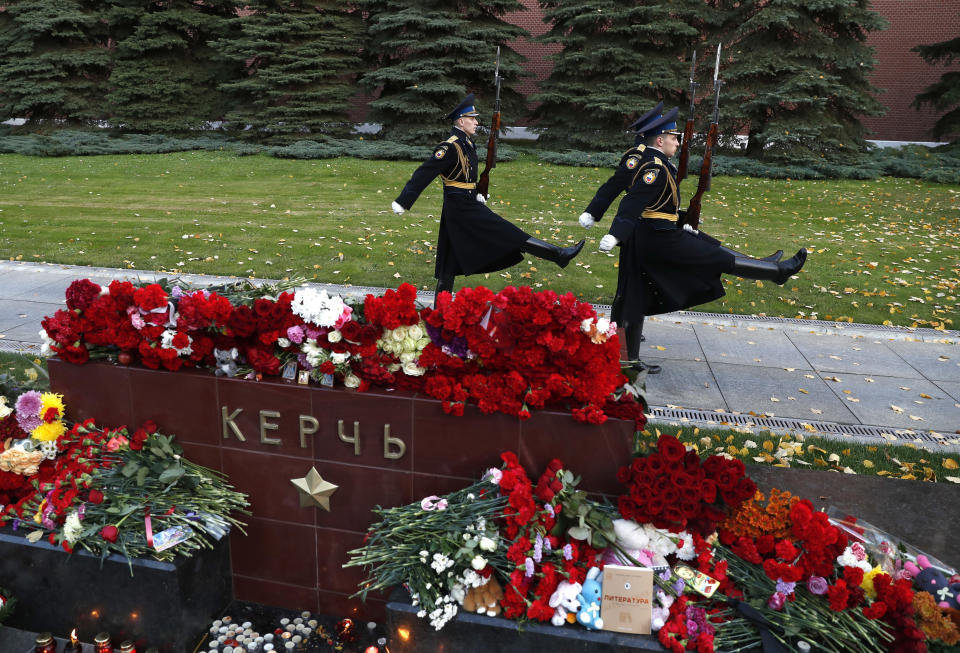 Guardias del Kremlin marchan frente a flores colocadas para las víctimas del ataque del miércoles en un instituto vocacional en Kerch, Crimea, con una lápida con la palabra Kerch en el jardín Alexander cerca del Kremlin, Moscú, Rusia, el jueves 18 de octubre de 2018. (AP Photo/Pavel Golovkin)