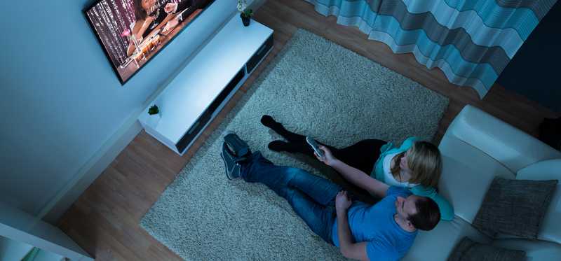 Couple watching tv in a darkened living room.