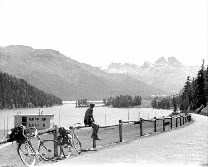 A bicycle tour of the Alps in the 1940s by a lake.