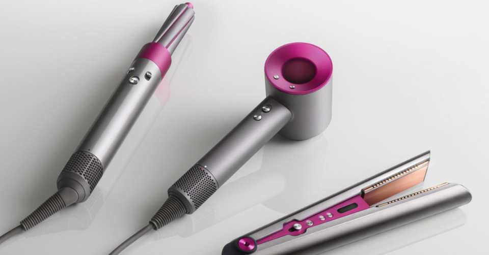 Three Dyson products in pink and silver including a wand, a dryer and a straightener.