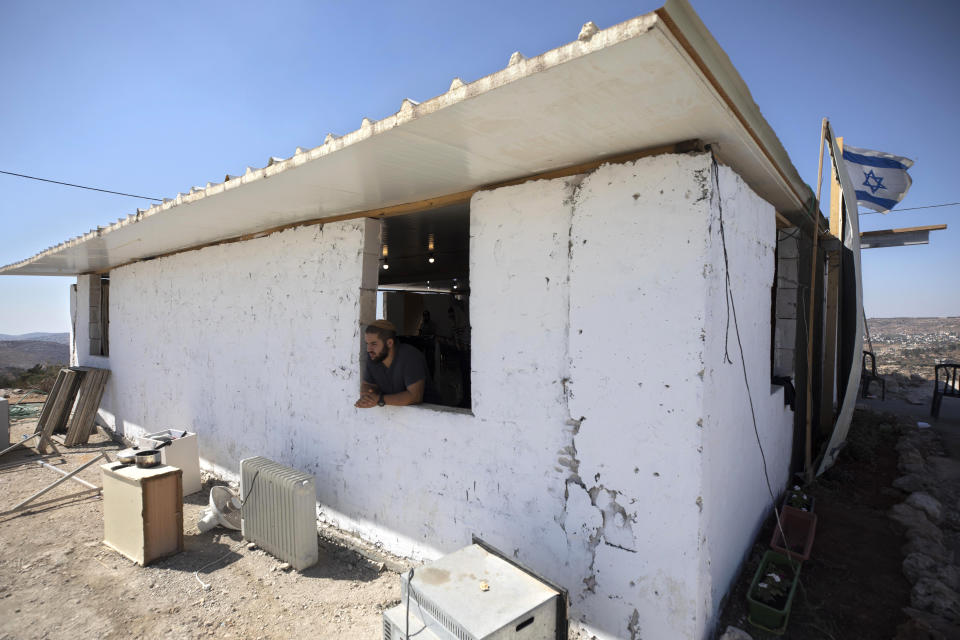 An Israeli settler looks out of a window at the outpost of Eviatar near the northern West Bank town of Nablus, Monday, June 21, 2021. Settlers established the outpost last month and say it is now home to dozens of families. Palestinians say it is built on private land and fear it will grow and merge with other large settlements nearby. (AP Photo/Sebastian Scheiner)