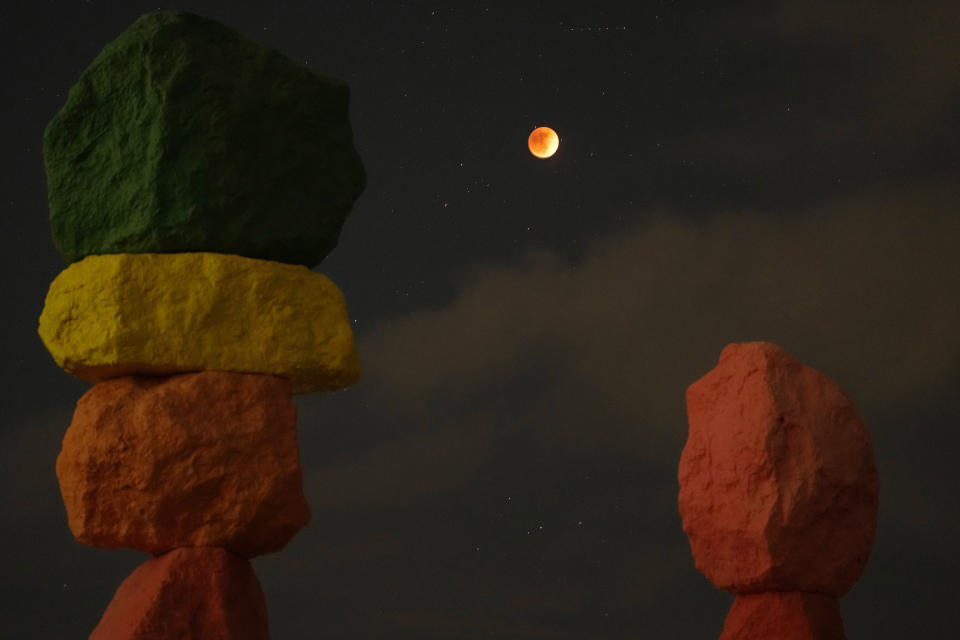 A lunar eclipse is seen above the artwork titled: "Seven Magic Mountains" by artist Ugo Rondinone, during the first blood moon of the year Sunday, May 15, 2022, near Jean, Nev. (AP Photo/John Locher)