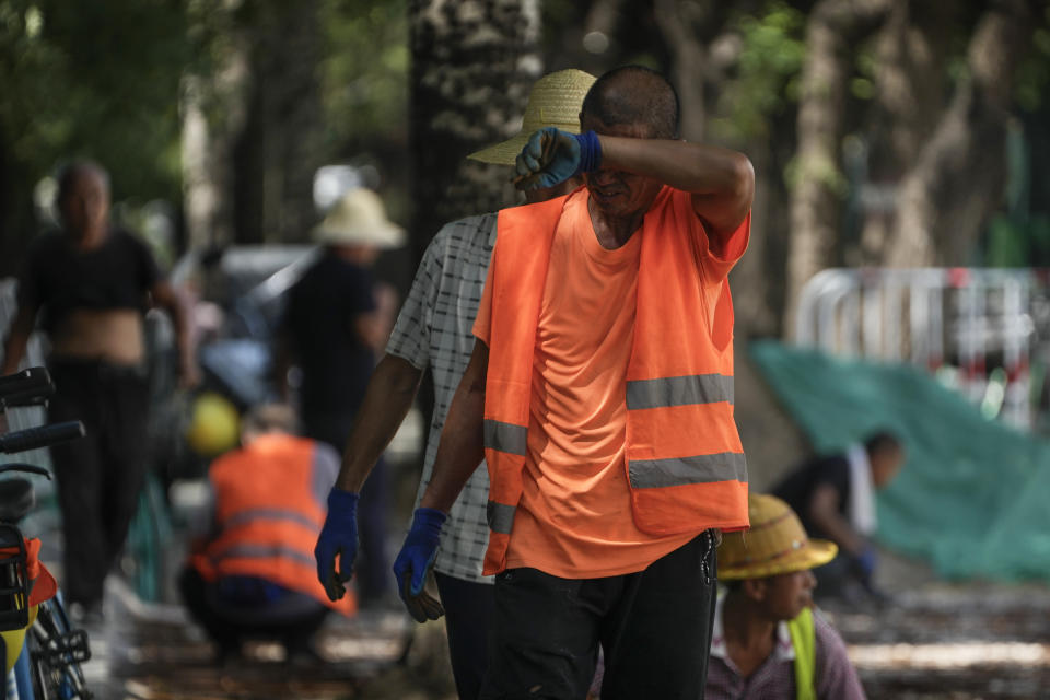 A worker wipes his sweat as he and his co-workers place tiles on a pavement on a sweltering day in Beijing, Monday, July 10, 2023. Rescuers were looking Monday for several people missing in a landslide triggered by torrential rains while employers across much of China were ordered to limit outdoor work due to scorching temperatures as the country struggled with heat, flooding and drought. (AP Photo/Andy Wong)