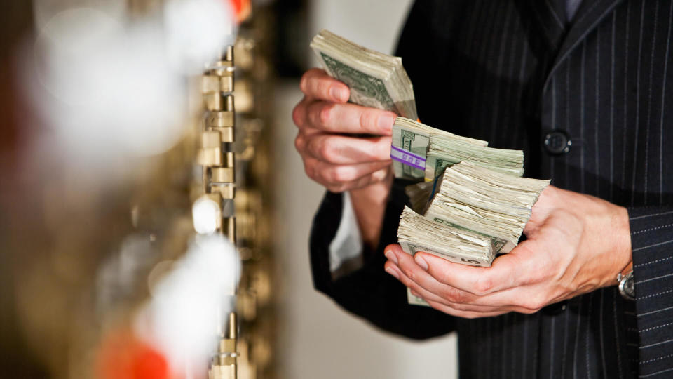 Man holding big stack of US paper currency by safety deposit boxes.