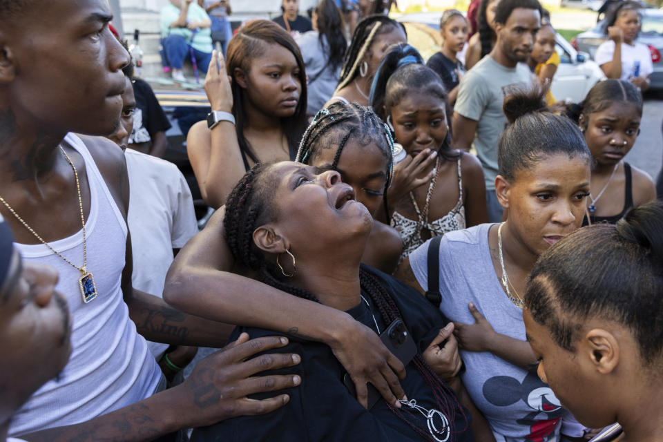 Friends and family comfort Antonio Lee's mother as she mourns her son at a vigil, Friday, Aug. 18, 2023, in Baltimore. Lee, 19, was shot and killed while squeegeeing in Baltimore. Two kids named Antonio grew up together in the streets of east Baltimore surrounded by poverty and gun violence. But only one would make it out alive. Antonio Moore is a successful real estate investor and marketing consultant. His friend Antonio Lee was shot and killed last summer, four months before his 20th birthday. (AP Photo/Julia Nikhinson)