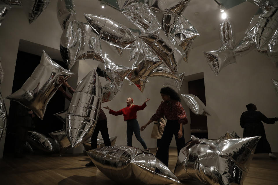 Tate representatives pose for photographs by interacting with the Andy Warhol piece "Silver Clouds" 1966, reprint 1994 helium-filled metalised plastic film (Scotchpak) during a media preview for the exhibition "Andy Warhol" at the Tate Modern gallery in London, Tuesday, March 10, 2020. The exhibition, which runs from March 12 to September 6, features over 100 works spanning the American artist's career in the second half of the 20th century until his death in 1987. (AP Photo/Matt Dunham)