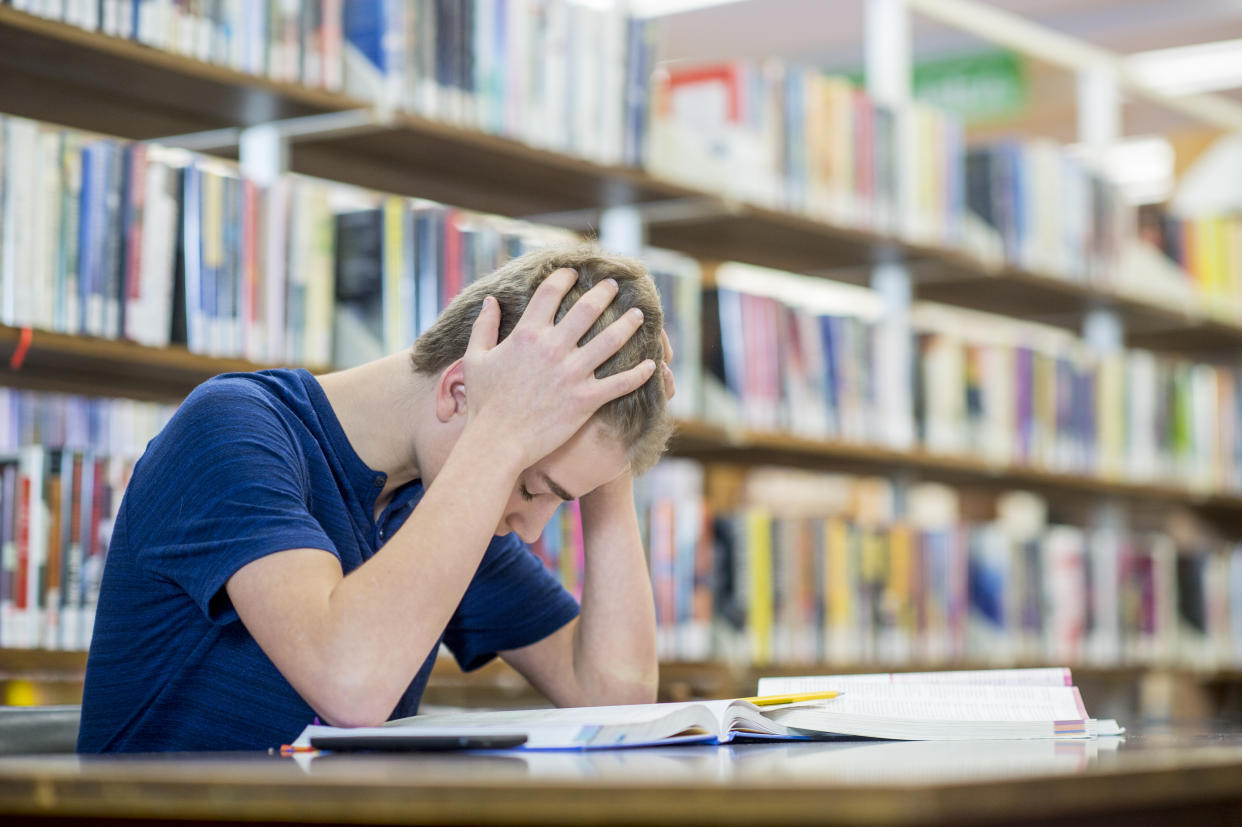 A teenage student holds his heads while studying in a library.