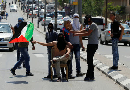 A protester waves a Palestinian flag as he sits on a chair during clashes with Israeli troops following a protest in solidarity with Palestinian prisoners held by Israel, in the West Bank town of Bethlehem April 17, 2017. REUTERS/Ammar Awad