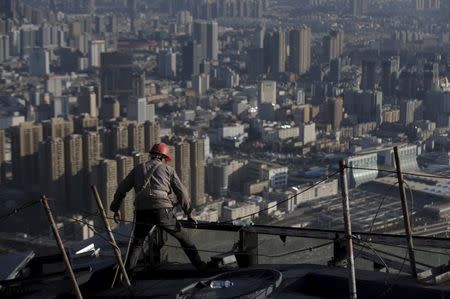 A labourer works atop a construction site of a commercial building as residential complexes are pictured in the background, in Kunming, Yunnan province, China, December 12, 2015. REUTERS/Wong Campion