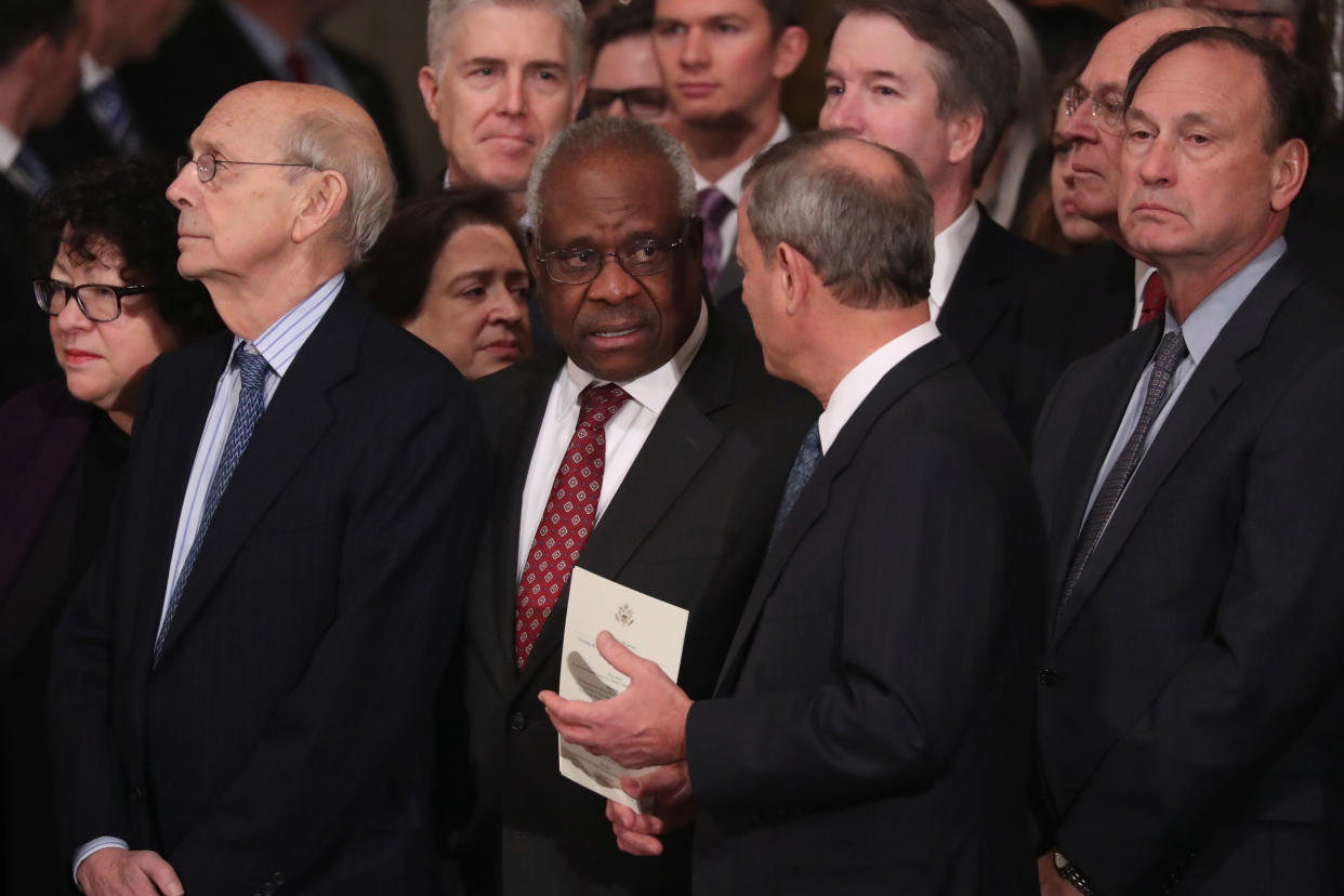 Supreme Court justices all stand, including Clarence Thomas, who is in conversation with Chief Justice John Roberts.