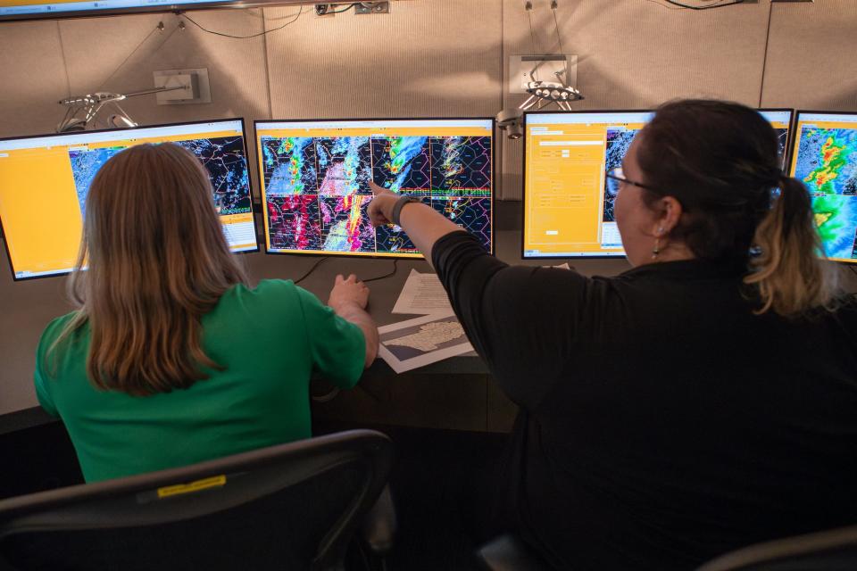 Two people sit at desks with their backs to the camera facing several computers with storm warnings on the screens