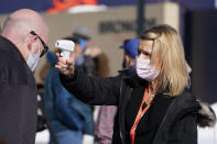 Rachel Deets, right, special events assistant for the Denver Broncos, uses a thermometer to take the temperature of beat writer Ryan O'Halloran before he can watch the team take part in drills during an NFL football practice at the team's headquarters Wednesday, Nov. 25, 2020, in Englewood, Colo. (AP Photo/David Zalubowski)