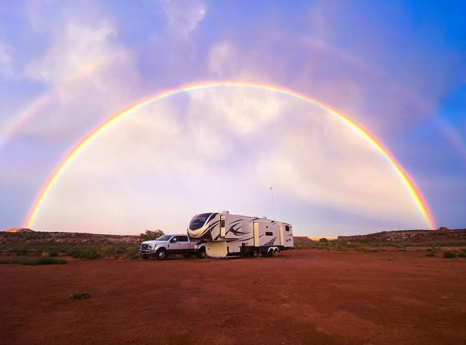 A picture of the couple's RV outdoors in a large empty field with a rainbow in the background.