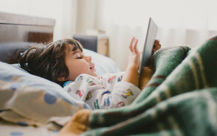 a little kid laying in bed on his ipad