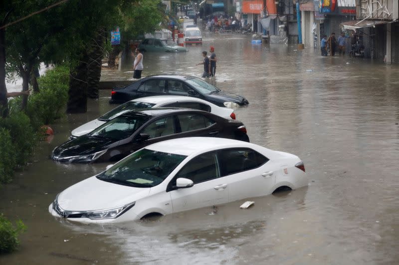 People wade through a flooded street with submerged vehicles during the monsoon rain, as the outbreak of the coronavirus disease (COVID-19) continues, in Karachi