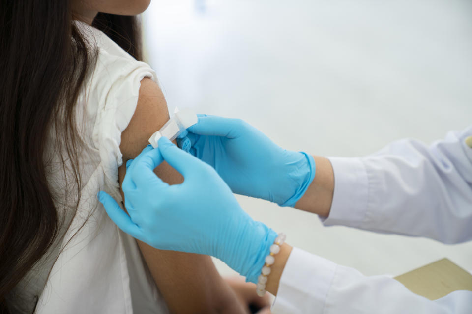 A healthcare professional wearing gloves applies a band-aid to a person's arm after a vaccination