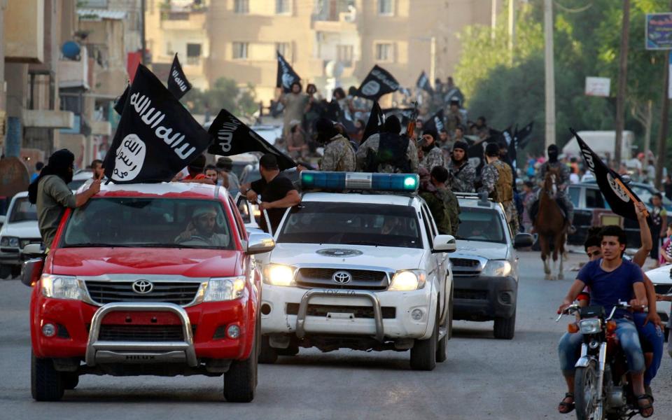 Islamic State fighters wave flags on a military parade in Raqqa province - Reuters