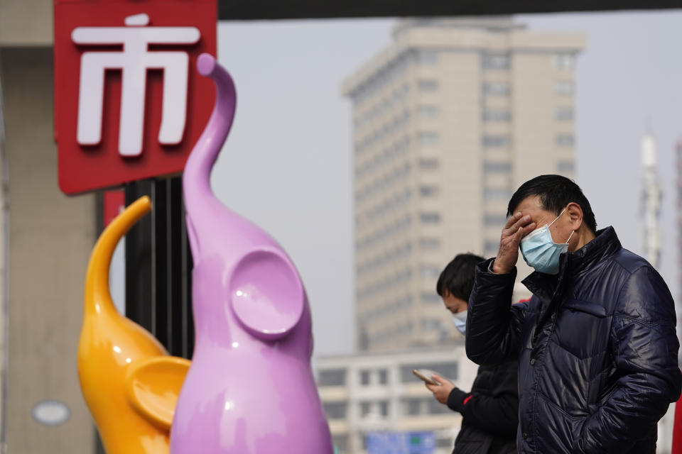 Residents wearing masks to curb the spread of the coronavirus stand near the Chinese character for "Market" in Wuhan, China, Tuesday, Jan. 26, 2021. The central Chinese city of Wuhan, where the coronavirus was first detected has largely returned to normal but is on heightened alert against a resurgence as China battles outbreaks elsewhere in the country. (AP Photo/Ng Han Guan)