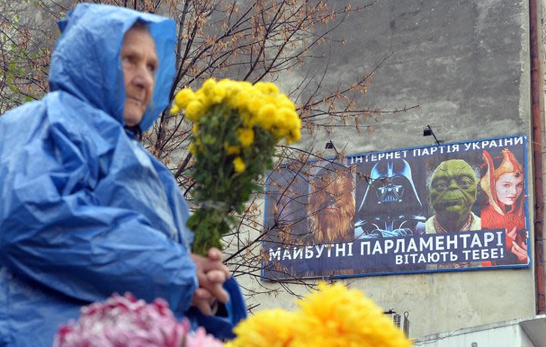 A woman sells flowers on October 23, 2014 in front of a campaign billboard of the Internet Party of Ukraine, in the market in Lviv