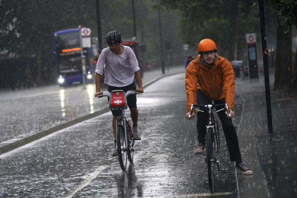 Two cyclists ride along the Embankment in central London, Sunday July 25, 2021. Thunderstorms bringing lightning and torrential rain to the south are set to continue until Monday it is forecast. (Victoria Jones/PA via AP)