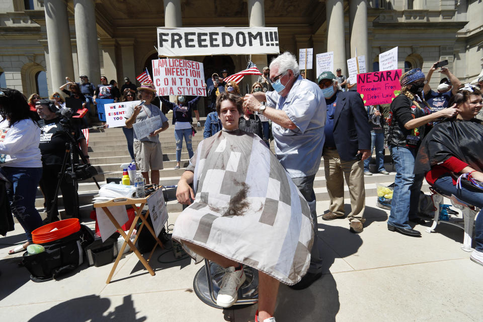 Barber Karl Manke, of Owosso, gives a free haircut to Parker Shonts on the steps of the State Capitol during a rally in Lansing, Mich., Wednesday, May 20, 2020. from the new coronavirus COVID-19. Barbers and hair stylists are protesting the state's stay-at-home orders, a defiant demonstration that reflects how salons have become a symbol for small businesses that are eager to reopen two months after the COVID-19 pandemic began. (AP Photo/Paul Sancya)