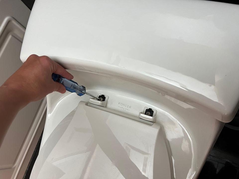 Using a screwdriver to unscrew a toilet seat for replacement.