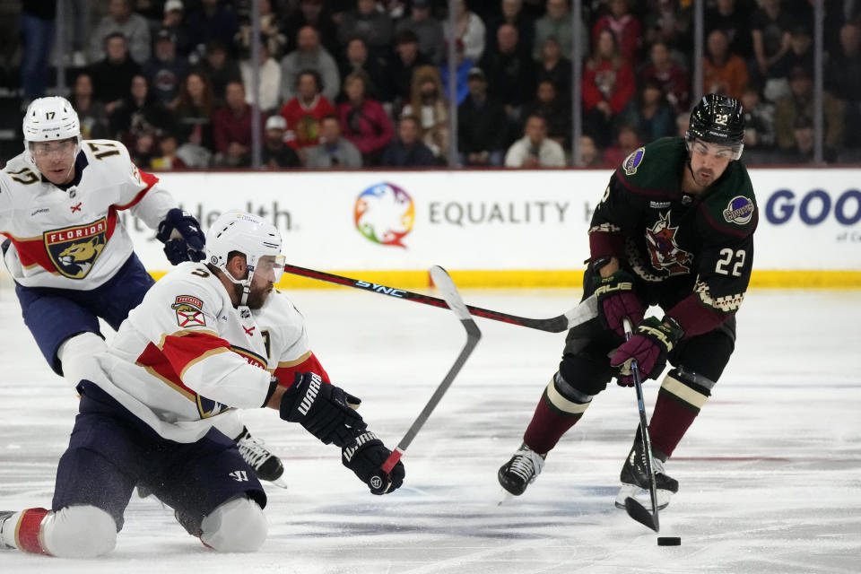 Arizona Coyotes center Jack McBain (22) passes the puck as Florida Panthers defenseman Aaron Ekblad, second from left, slides across the ice while Panthers center Evan Rodrigues (17) looks on during the first period of an NHL hockey game Tuesday, Jan. 2, 2024, in Tempe, Ariz. (AP Photo/Ross D. Franklin)