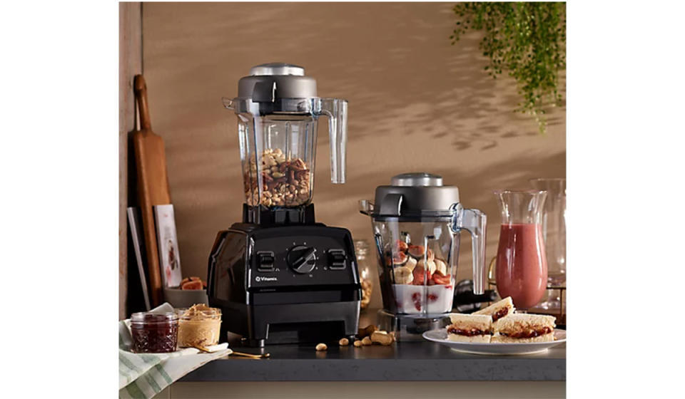 Vitamix Explorian on counter with dry nuts in the blender cup and a second cup on the counter with unblended smoothie ingredients. 