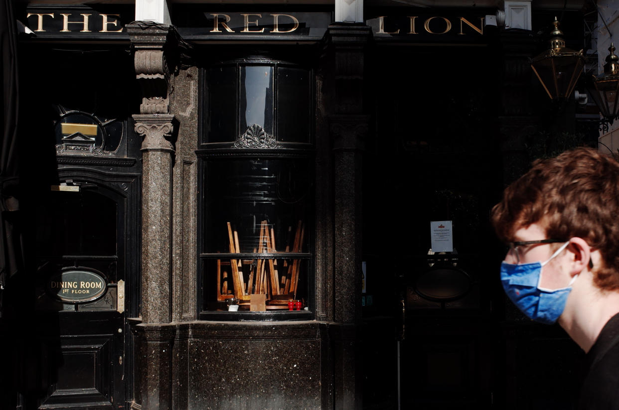 A man wearing a face mask walks past upturned stools in the window of The Red Lion pub, closed due to coronavirus, on a near-deserted Whitehall in London, England, on May 28, 2020. The UK is now in its tenth week of coronavirus lockdown, with total deaths now standing at 37,837, according to today's updated count from the Department of Health and Social Care. British Prime Minister Boris Johnson meanwhile remains under unrelenting pressure over his refusal to sack his top aide, Dominic Cummings, who stands accused of flouting strict stay-at-home instructions by driving with his wife and son from London to County Durham on March 27 to stay at a family property. The reporting of the journey, and that of a subsequent trip to the Durham market town of Barnard Castle, has provoked huge public outcry since the story broke last Friday. (Photo by David Cliff/NurPhoto via Getty Images)