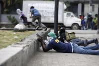 Armed off-duty police officers take cover during and exchange of gunfire with army soldiers during a protest over police pay and working conditions, in Port-au-Prince, Haiti, Sunday, Feb. 23, 2020. Off-duty police officers and their supporters exchanged fire for nearly two hours with members of the newly reconstituted Haitian army in front of the national palace. (AP Photo/Dieu Nalio Chery)