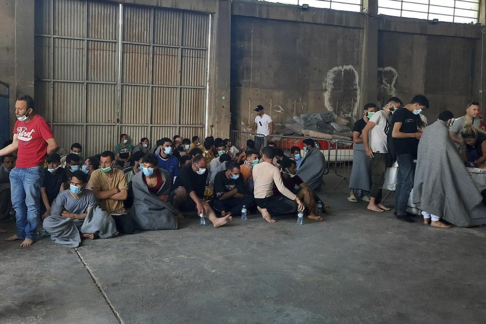 Survivors of a shipwreck sit at a warehouse at the port in Kalamata town, about 240 kilometers (150miles) southwest of Athens on Wednesday, June 14, 2023. Authorities say at least 30 people have died after a fishing boat carrying dozens of migrants capsized and sank off the southern coast of Greece. A large search and rescue operation is underway. (www.argolikeseidhseis.gr via AP)