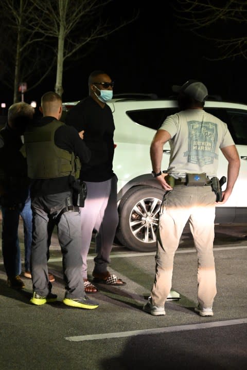 Deputies with the Walton County Sheriff's Office arresting Terrance George Owens in a parking lot. Owens is wearing a mask and is being handcuffed. Two deputies are standing behind him and one is standing infront of him. A white car is in the background of the photo.