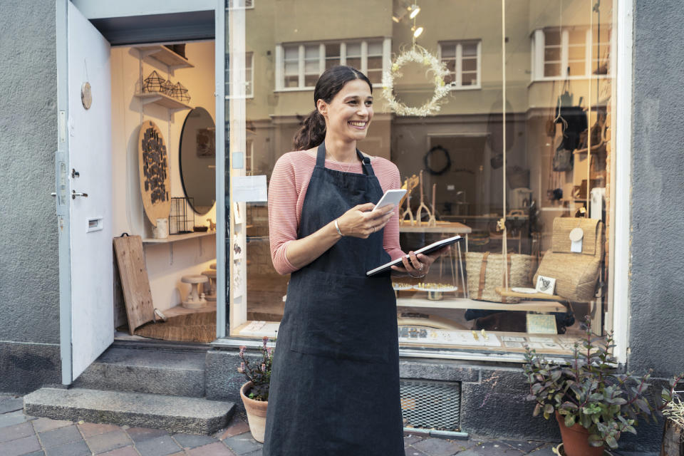 Smiling female entrepreneur with smart phone and digital tablet outside store