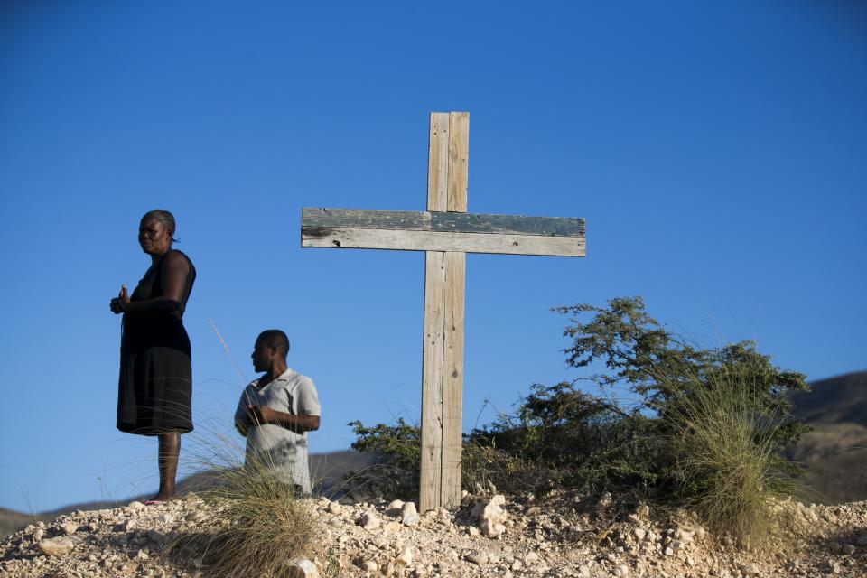 Residents stand next to a cross during a memorial service honoring the victims of the 2010 earthquake, at Titanyen, a mass burial site north of Port-au-Prince, Haiti, Sunday, Jan. 12, 2020. Sunday marks the 10th anniversary of the devastating 7.0 magnitude earthquake that destroyed an estimated 100,000 homes across the capital and southern Haiti, including some of the country's most iconic structures. (AP Photo/Dieu Nalio Chery)