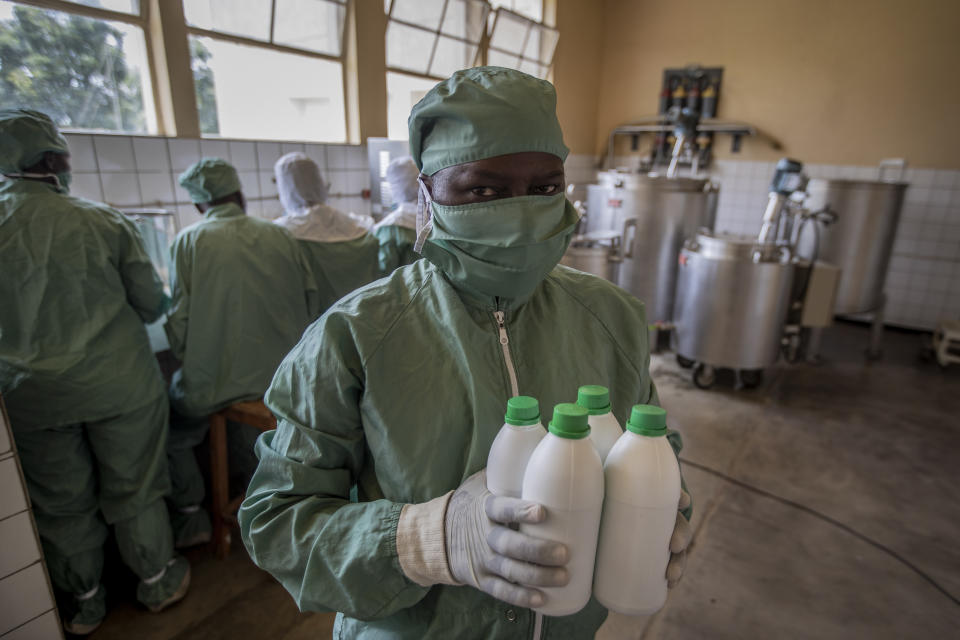 In this photo taken Thursday, Nov. 7, 2019, a worker carries bottles of liquid morphine after making it from powder, wearing protective clothing to protect from the effects of the drug and to prevent contamination, at the Pharmaceutical Laboratory of Rwanda in Butare, Rwanda. While people in rich countries are dying from overuse of prescription painkillers, people in Rwanda and other poor countries are suffering from a lack of them, but Rwanda has come up with a solution to its pain crisis - it's morphine, which costs just pennies to produce and is delivered to households across the country by public health workers. (AP Photo/Ben Curtis)