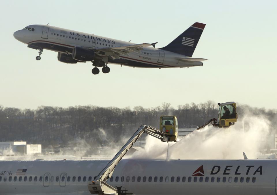 A Delta jetliner (bottom) is de-iced while a US Airways jet takes off at Reagan National Airport in Washington January 3, 2014. A heavy snowstorm and dangerously cold conditions gripped the northeastern United States on Friday, delaying flights, paralyzing road travel and closing schools and government offices across the region. REUTERS/Gary Cameron (UNITED STATES - Tags: ENVIRONMENT TRANSPORT TRAVEL)