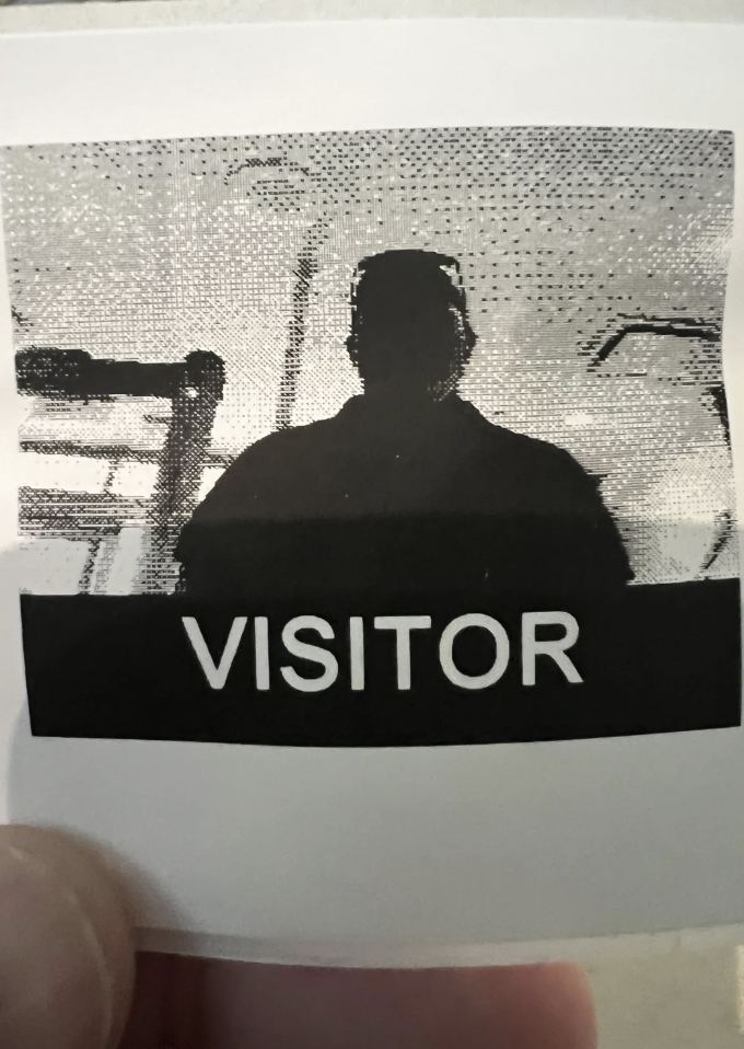 Silhouetted figure on a visitor badge held by a person's hand