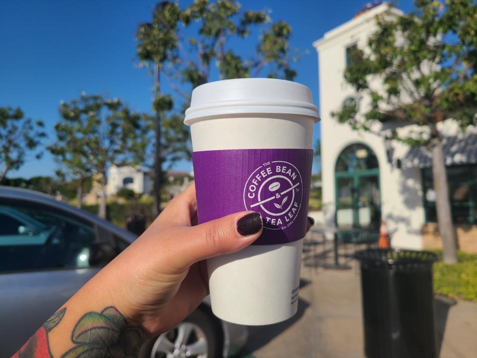 A Coffee Bean & Tea Leaf cup being held up by a woman's hand in front of a Coffee Bean & Tea Leaf storefront.