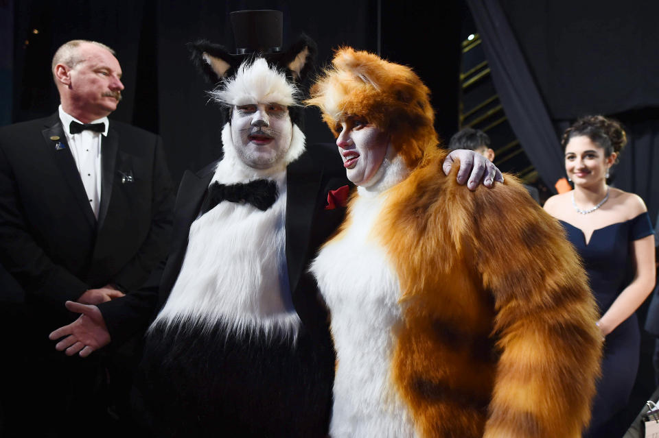 Two people in elaborate 'Cats' musical costumes with theatrical makeup, posing with others at an event