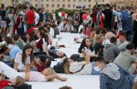 People sit on a white canvas in front of government building in Minsk, Belarus, Saturday, Aug. 15, 2020. Tens of thousands of people have flooded the heart of the Belarus capital of Minsk in a show of anger over a brutal police crackdown this week on peaceful protesters that followed a disputed election. (AP Photo/Dmitri Lovetsky)