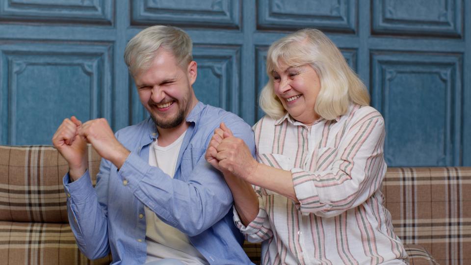 Smiling young man with gray-haired old mom or grandmother dancing, laughing. Good friends. Happy bonding loving generations family of senior mother and handsome adult son or grandson moving in dance