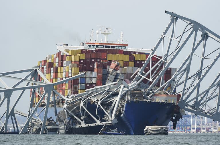 Un guardacostas pasa junto a un buque de carga que está atrapado debajo de la parte de la estructura del puente Francis Scott Key después de que el barco llegó al puente el martes 26 de marzo de 2024 en Baltimore (Foto AP/Steve Helber)