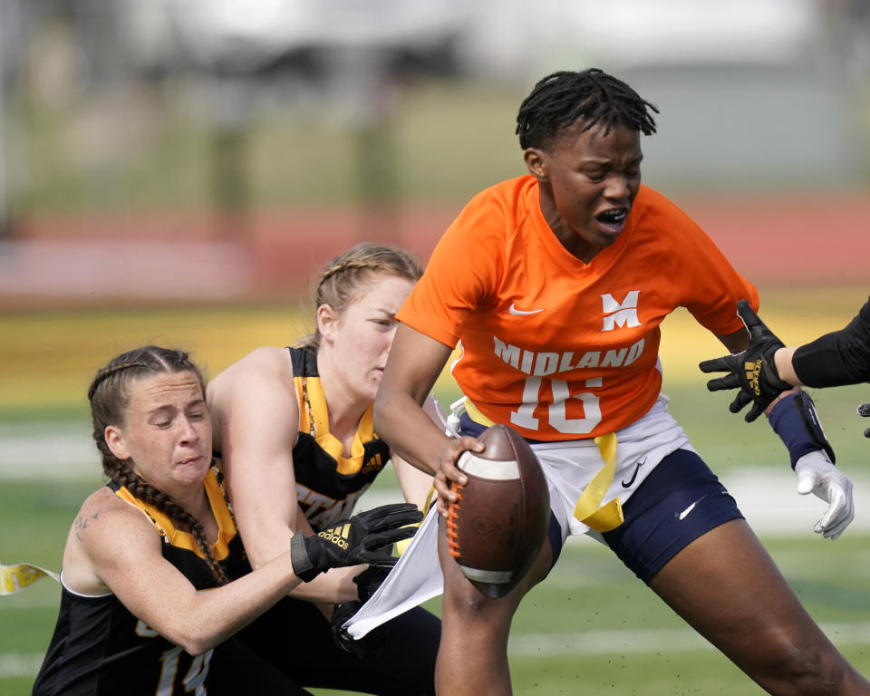 Midland quarterback E'leseana Patterson (16) is tackled by Ottawa defenders Jeffifer Anthony, left, and Courtney Wille during an NAIA flag football game in Ottawa, Kan., Friday, March 26, 2021. The National Association of Intercollegiate Athletics introduced women's flag football as an emerging sport this spring. (AP Photo/Orlin Wagner)