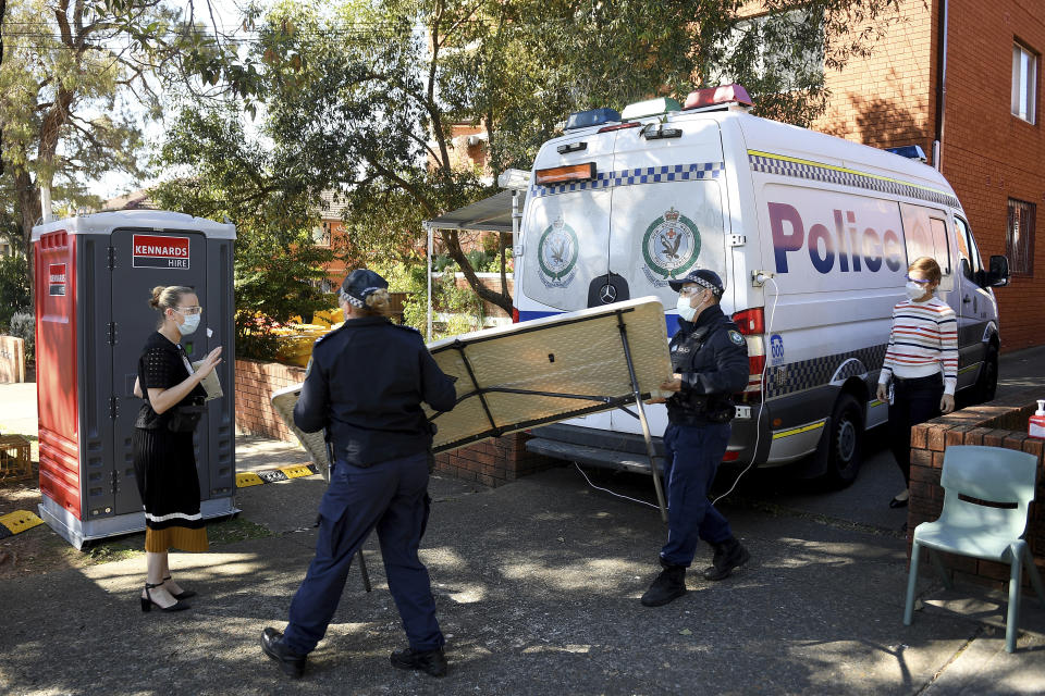 Health workers and police officers are seen at a unit block under lockdown in Campsie, southwest of Sydney, Friday, Aug. 20, 2021. A lockdown in Australia's largest city was extended throughout September and tougher measures to curb the coronavirus's delta variant were imposed Friday, including a curfew and a mask mandate outdoors. (Dan Himbrechts/AAP Image via AP)