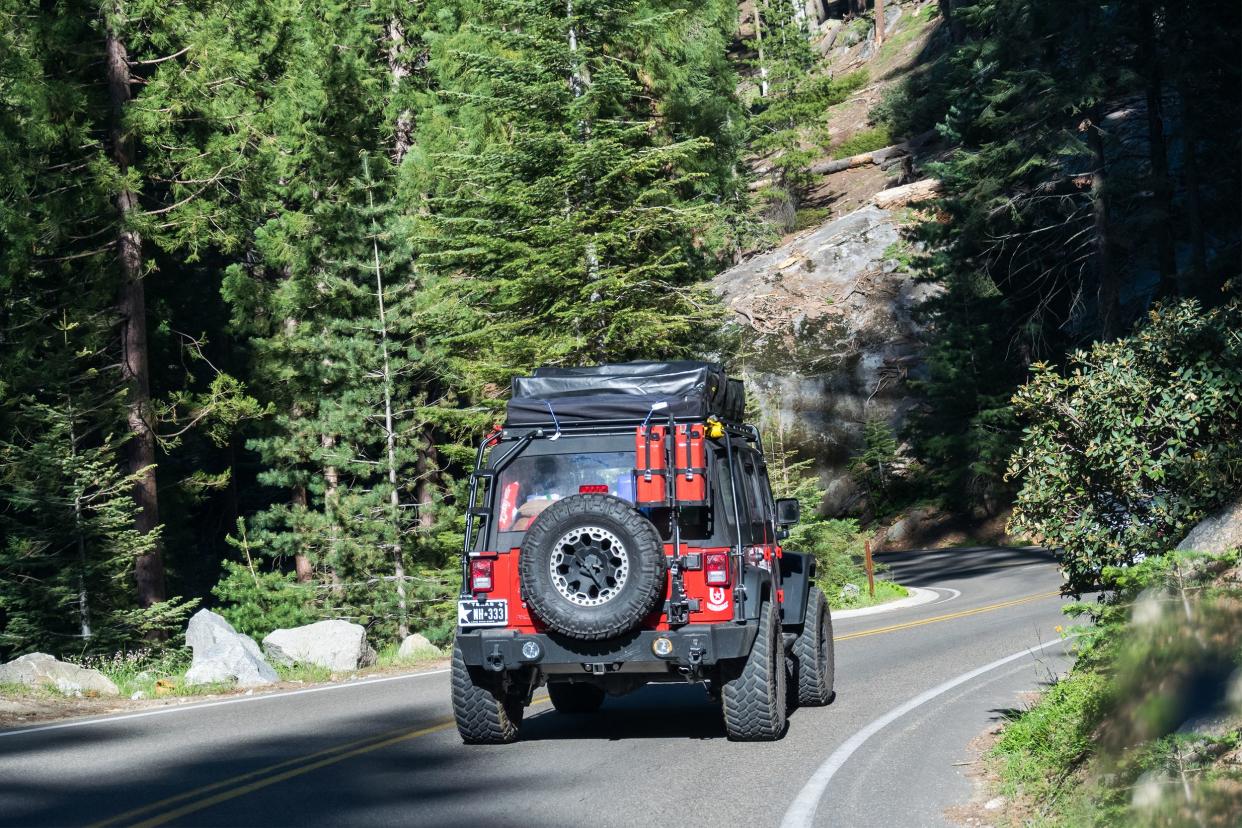 Loaded up red Jeep driving on a winding mountain road on a sunny day.