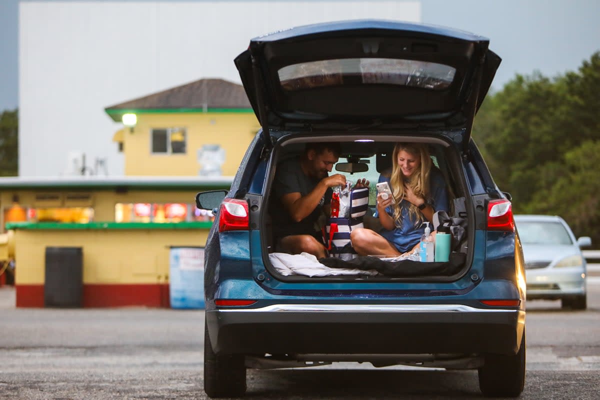 Two people get situated to watch a movie at a drive-in movie theater. 