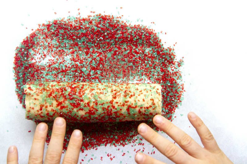 someone rolling dough in sprinkles with their hands