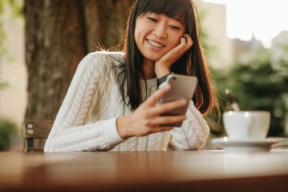 Asian woman smiles at her smartphone.