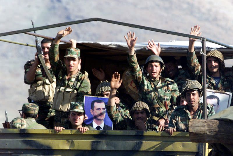 FILE PHOTO: Syrian army troops wave from truck driving towards the Lebanese Syrian border in the Bekaa valley.