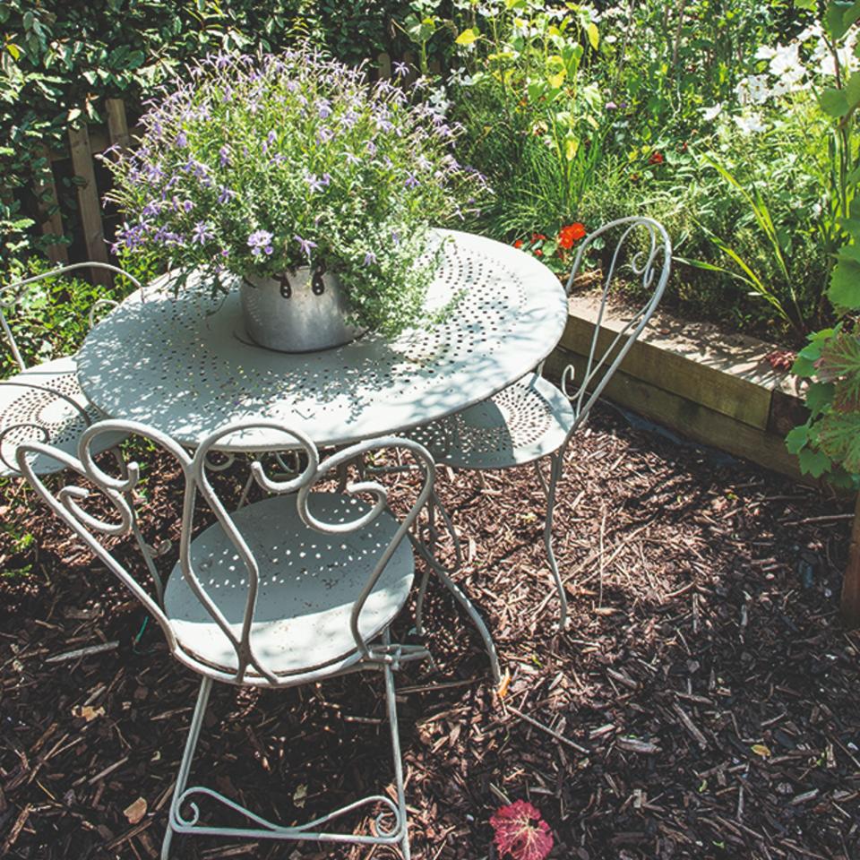 A garden with a garden furniture set and a flowering plant on top and all around